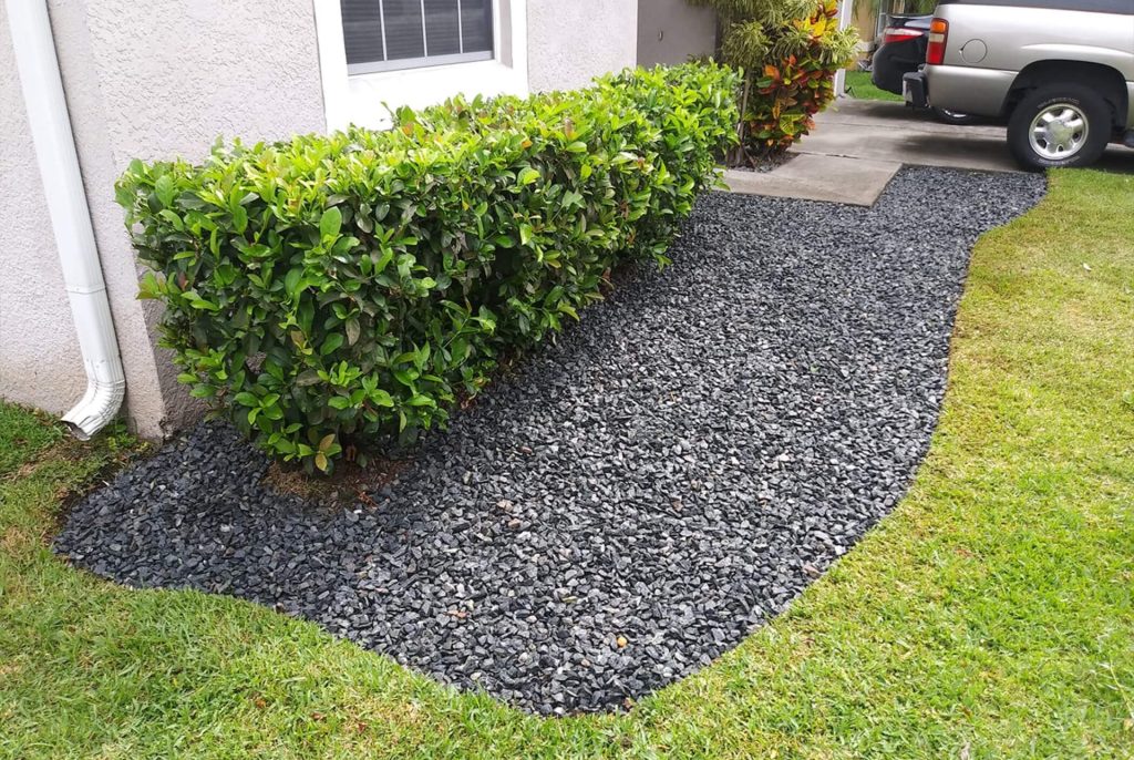 A granite rock garden bed in San Diego, extending from the walkway across the front of the house, with a hedge growing in it